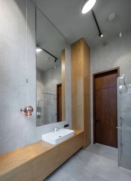 Interno del bagno in appartamento di lusso. Design grigio e legno. Lavello bianco. — Foto Stock