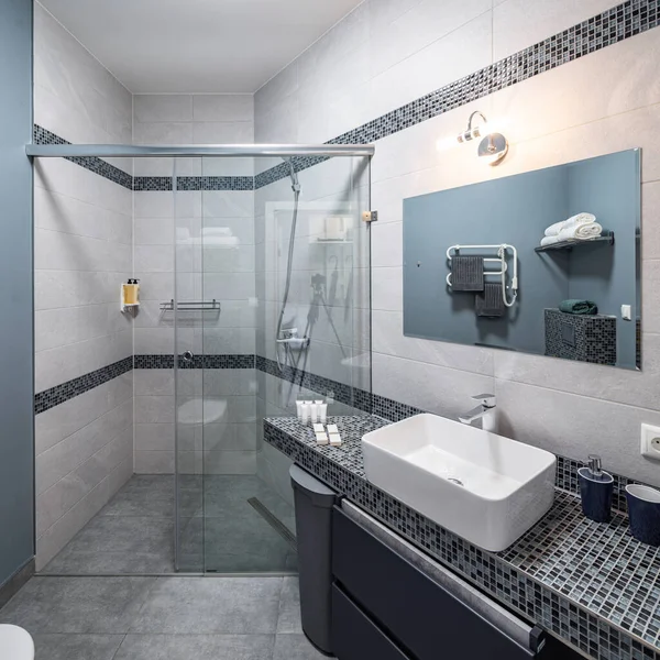Modernes Interieur des Badezimmers in einer Luxuswohnung. Dusche aus Glas vorhanden. Weißes Waschbecken. Graue Fliese. — Stockfoto