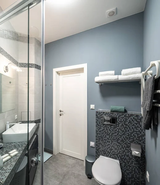 Modernes Interieur des Badezimmers in einer Luxuswohnung. Dusche aus Glas vorhanden. Weißes Waschbecken und Toilette. Graue Fliese. — Stockfoto