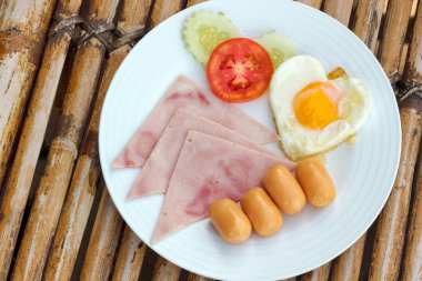 plaka ile bir bambu tablo klasik Kızarmış sosis, jambon ve yumurta kahvaltı