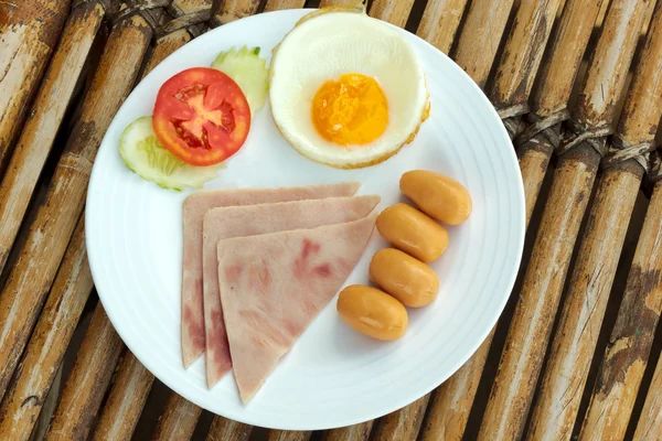 Prato com ovo frito clássico, presunto e salsicha café da manhã em uma mesa de bambu — Fotografia de Stock