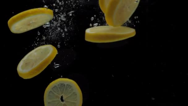 Повільний рух скибочок лимона, що падає у прозорій воді на чорному тлі — стокове відео