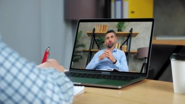 Ofisteki adam deftere yazıyor. Yönetmen video görüntülü bilgisayarı arıyor.