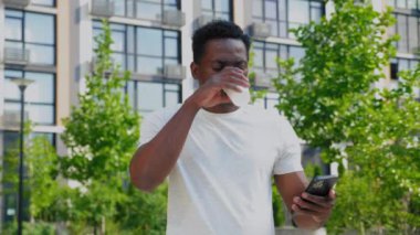 Afro-Amerikalı serbest çalışan adam yazın akıllı telefon kullanır ve kahve içer.