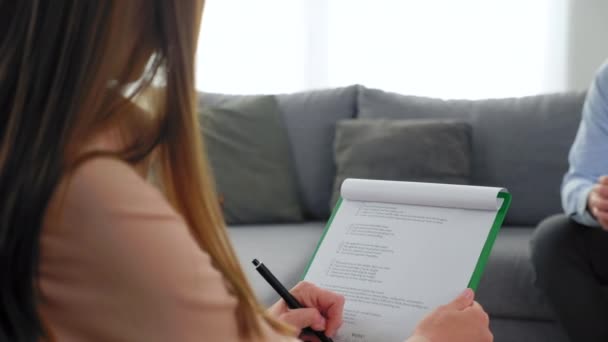 Psychologist listens patient taking notes on clipboard at psychotherapy session — Stock Video