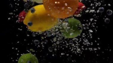 Yavaş çekim karışık çilek, yabanmersini, limon, limon, turuncu, yarı yeşil ve kırmızı elma siyah arka planda şeffaf suya düşüyor. Taze böğürtlen ve akvaryuma sıçrayan meyveler. Sağlıklı yemek.