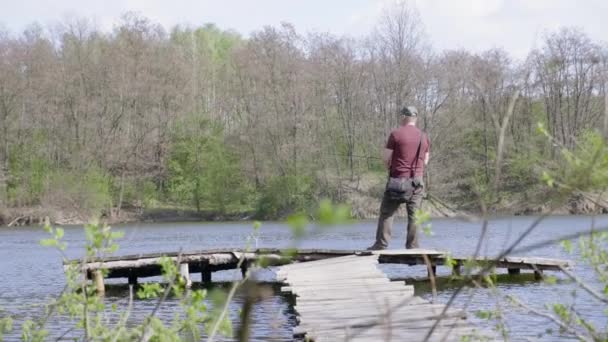 広いショット漁師は木製の橋の上に立っている間に魚をキャッチします 釣竿を持つ大人の男 — ストック動画