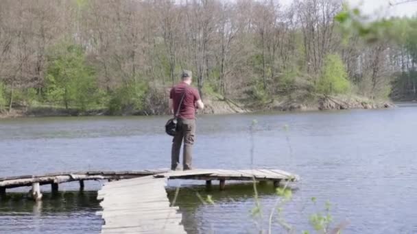 Pescador de tiro ancho captura peces mientras está de pie en un puente de madera — Vídeo de stock