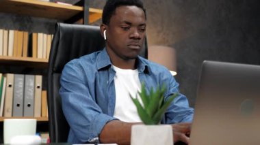 Kablosuz kulaklıklı Afrikalı Amerikalı adam klavyede dizüstü bilgisayar için çalışıyor.