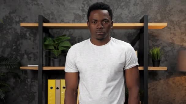 Afroamerikansk man tittar kamera och ler på bakgrund office inventering — Stockvideo