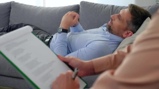 Дорослий чоловік з проблемами психічного здоров'я лежить на дивані, розмовляючи з терапевтом — стокове відео