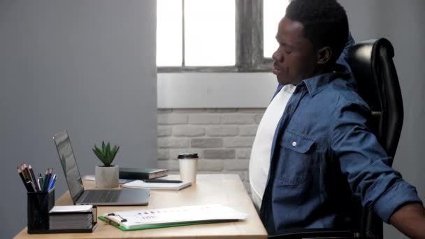 Fáradt afro-amerikai férfi nyújtja feszült izmok kemény munka után laptop — Stock videók