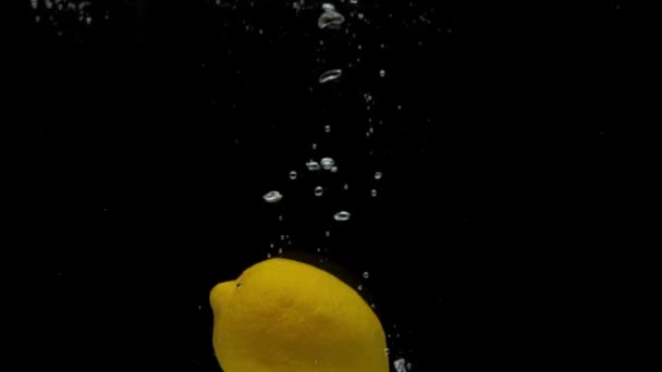 Limón amarillo de cámara lenta que cae en agua transparente sobre fondo negro — Vídeos de Stock