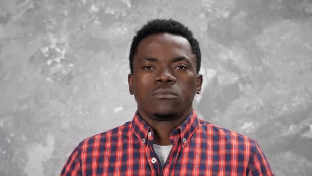 Vuxen afroamerikansk man tittar kamera, står på bakgrunden grå vägg — Stockvideo