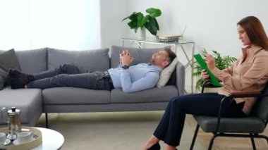 Akıl sağlığı sorunları olan yetişkin bir adam kanepeye uzanıp terapistle konuşuyor.