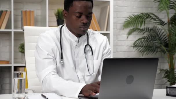 Afro-americano uomo medico digitando testo sul computer portatile tastiera in ambulatorio — Video Stock