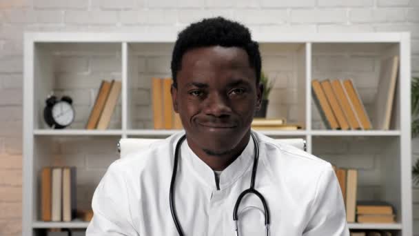 Sonriente hombre afroamericano doctor en abrigo médico mirando cámara en el hospital — Vídeos de Stock