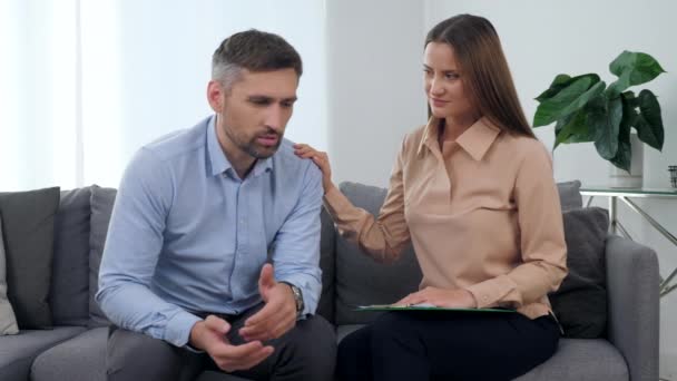 Szomorú férfi beteg beszél a problémájáról a női pszichológussal, aki támogatja. — Stock videók
