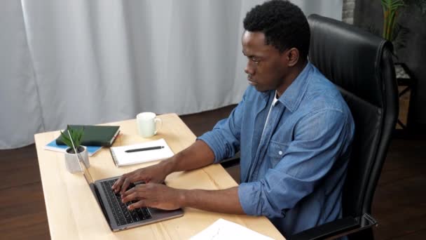 Афроамериканец работает на ноутбуке, печатая на клавиатуре в офисе — стоковое видео