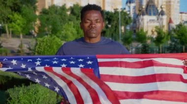 Vatansever Afro-Amerikalı adamın elinde Amerikan bayrağı var ve kameraya bakıyor.