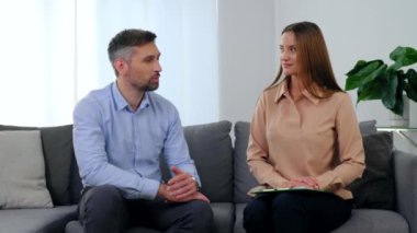 Erkek hasta ve kadın psikolog kanepede oturup konuşuyor ve kameraya dönüyor.