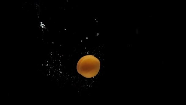 Slow motion aprikos spinning faller i transparent vatten på svart bakgrund — Stockvideo