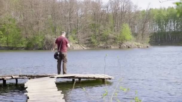 Weitschuss-Fischer fängt Fische, während er auf einer Holzbrücke steht — Stockvideo