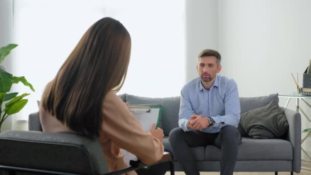 Uomo paziente con problemi di salute mentale seduto sul divano a parlare con il terapeuta — Video Stock