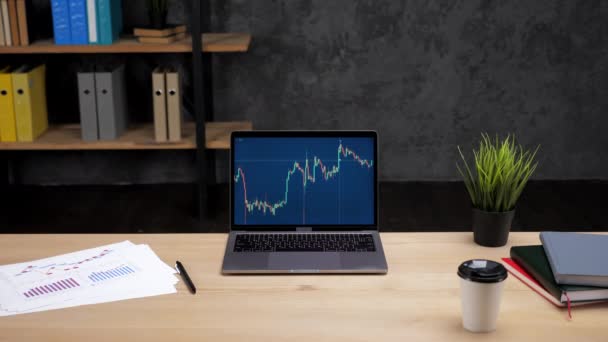 Laptop computer met grafiek van de beurs op het scherm staat op tafel in het kantoor — Stockvideo