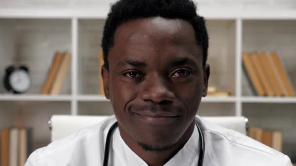 Крупным планом улыбающийся афроамериканец врач смотрит в камеру в больнице — стоковое видео