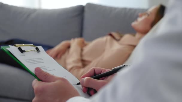 Mann in Großaufnahme Psychotherapeut macht Notizen auf Klemmbrett und hört Patientin zu — Stockvideo
