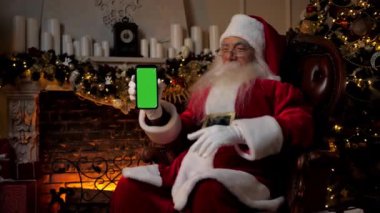 Modern gülümseyen Noel Baba akıllı telefon yeşil ekran kalemlerini gösteriyor.