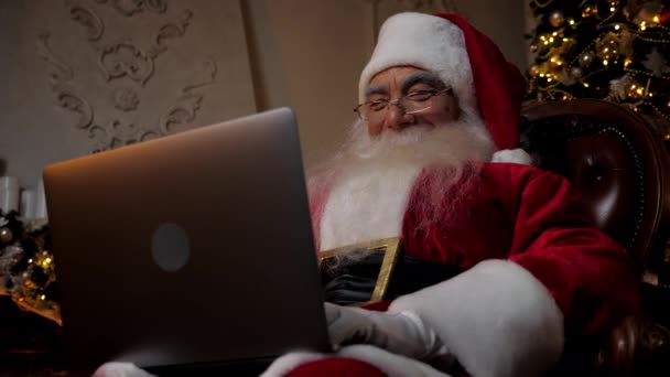 Χαμογελώντας σύγχρονο Santa Claus χρησιμοποιεί laptop γεμίζει τις κάρτες διακοπών για τα παιδιά — Αρχείο Βίντεο