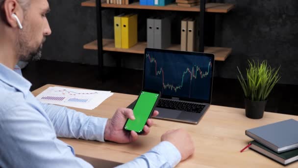 Man mäklare rulla grön skärm smartphone, bärbar dator med börsdiagram — Stockvideo