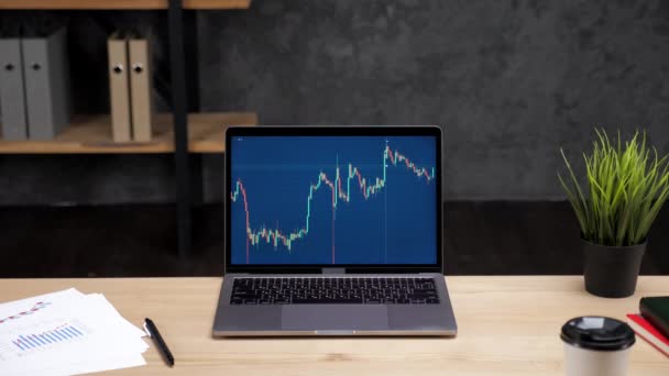 Bärbar dator med diagram över börsen på skärmen står på bordet på kontoret — Stockvideo