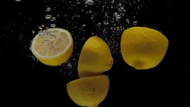 黒の背景に透明な水に落ちるスローモーションレモンの半分 — ストック動画
