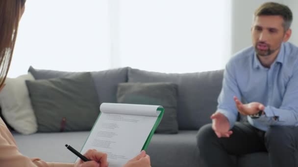 Homem sem foco com problemas de saúde mental sentado no sofá conversando com o terapeuta — Vídeo de Stock