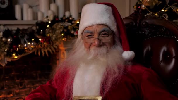 Close-up glimlachen kerstman looks looks camera zitten op stoel thuis — Stockvideo