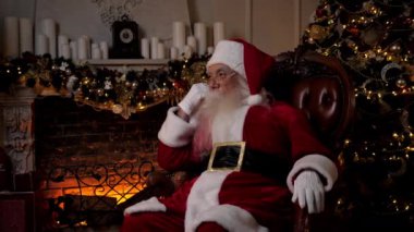 Düşünceli Noel Baba evdeki sandalyede otururken başka tarafa bakıyor. Noel tatili