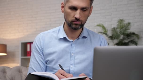 Close-up man handelaar makelaar luistert investeerder online laptop, notities in notebook — Stockvideo