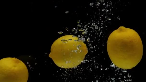 Slow motion yellow lemon falling into transparent water on black background — Stock Video