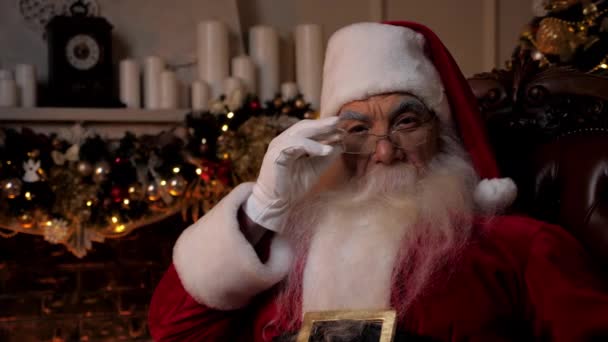 Close up Santa Claus vypadá kamera sedí na židli doma, vánoční prázdniny — Stock video