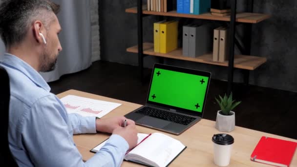 Ο χρηματιστής άνθρωπος κάνει σημειώσεις στο σημειωματάριο χρησιμοποιεί φορητό υπολογιστή με πράσινη οθόνη — Αρχείο Βίντεο