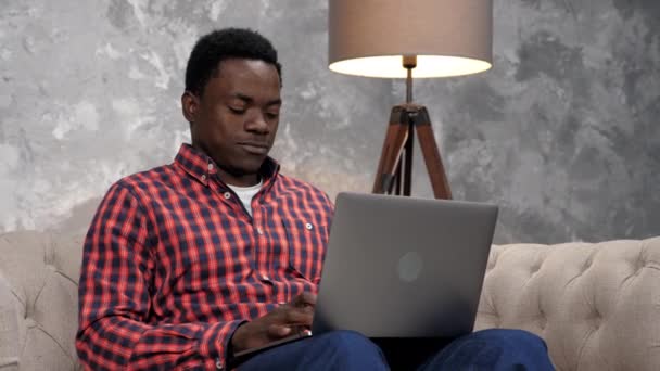笑着坐在沙发上工作的非裔美国人，用键盘打字 — 图库视频影像