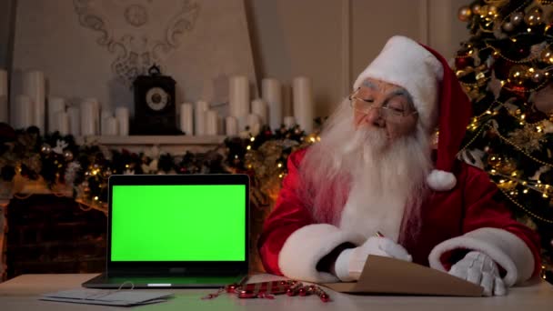 Санта-Клаус пишет поздравления детям с Новым годом, ноутбук зеленый экран — стоковое видео