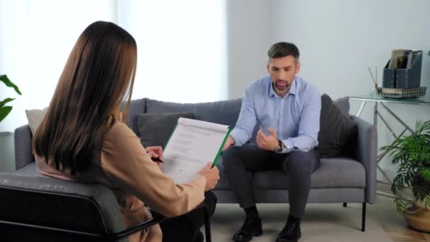 Psicólogo escucha cliente tomando notas en portapapeles en sesión de psicoterapia — Vídeos de Stock