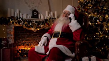 Modern gülümseyen Noel Baba, Noel tatillerinde çocuklarla cep telefonuyla konuşuyor.
