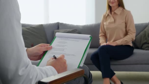 Primer plano psicoterapeuta hombre escucha paciente tomando notas en portapapeles en la clínica — Vídeo de stock