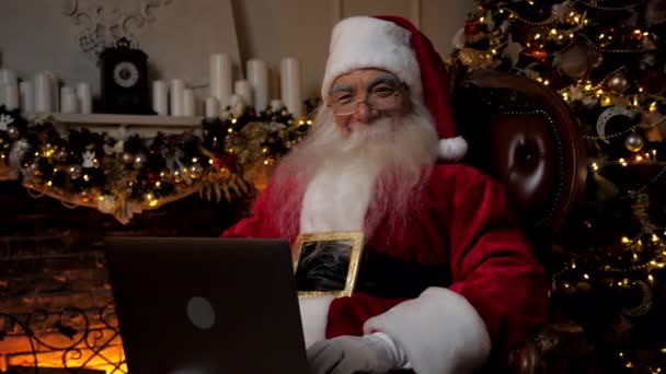 Moderner lächelnder Weihnachtsmann auf Stuhl sitzend Kamera nutzt Laptop-Computer — Stockvideo