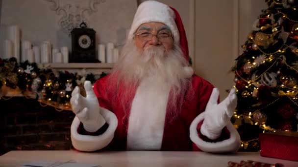 Śmiejący się Święty Mikołaj wygląda jak kamera siedząca na krześle przy biurku. Świąteczne wakacje — Wideo stockowe